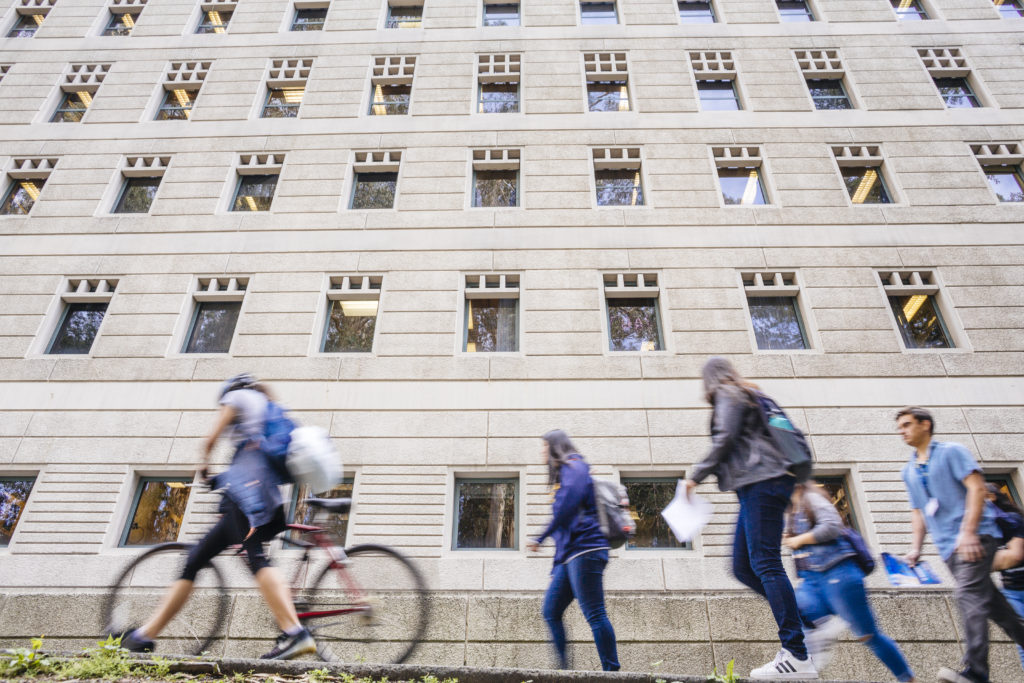 students walk and bike past a building