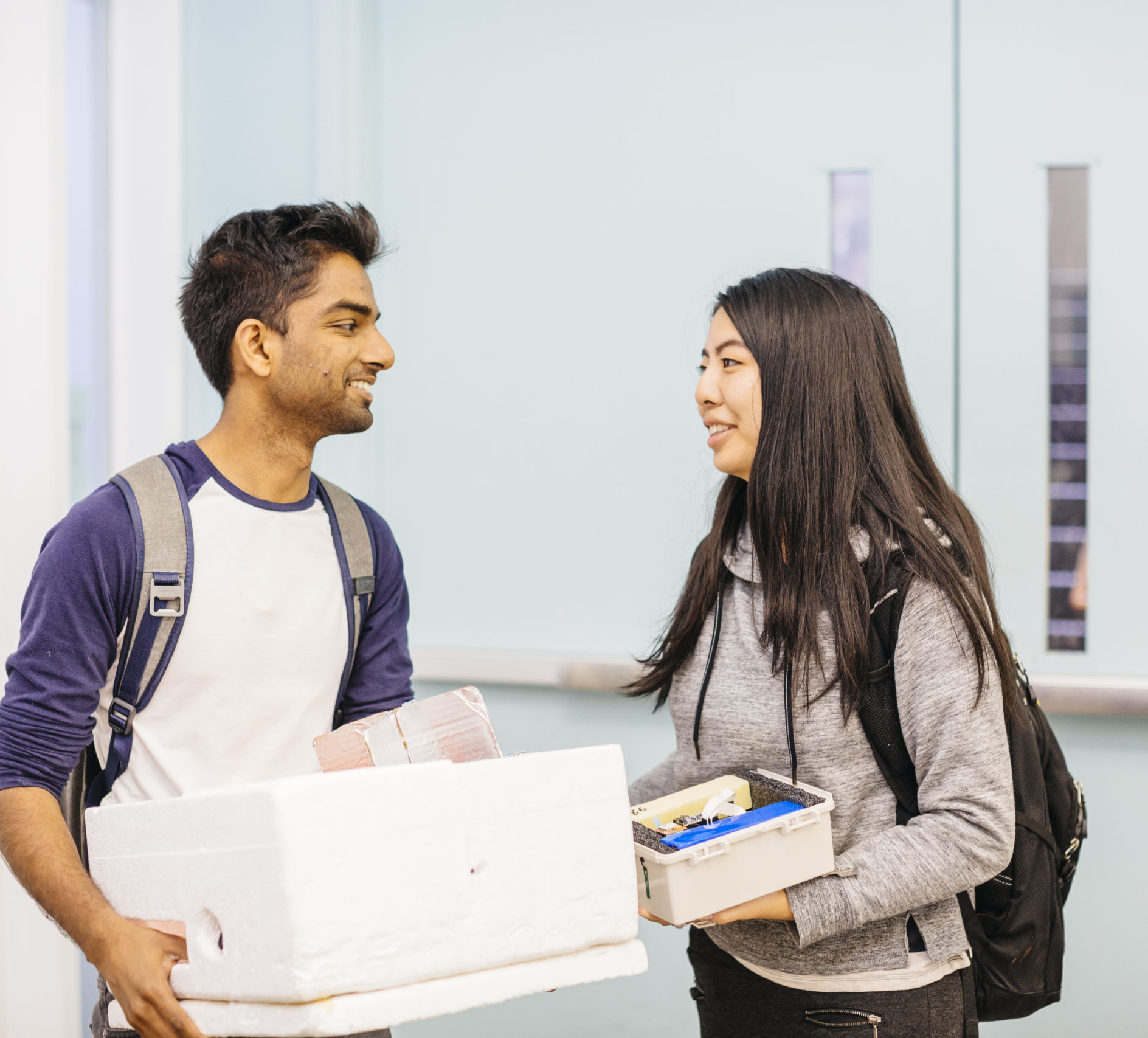 two students standing and talking; one is holding a box