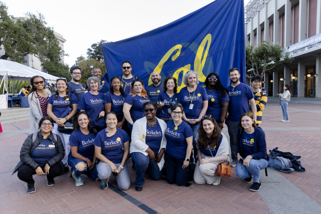 some graduate division staff members posing in front of Cal flag.