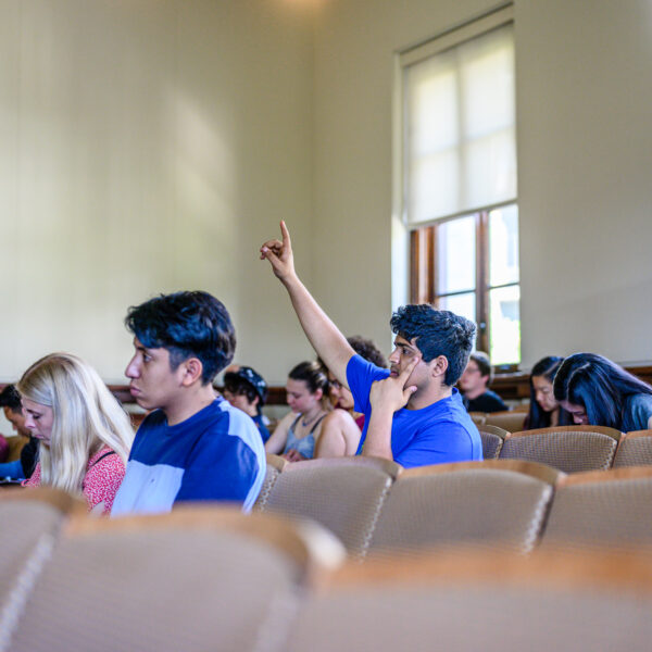 a student raising their hand while seated in a lecture hall.