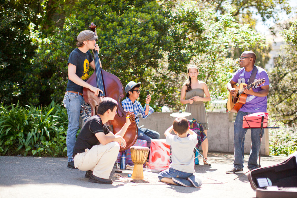 A group of seven students play musical instruments in a circle outdoors.