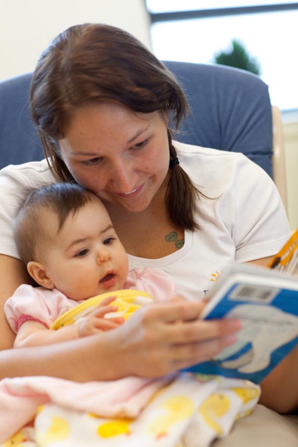 Image of caregiver reading a book to an infant