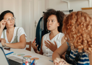 three women talking in front of a laptop and workstation