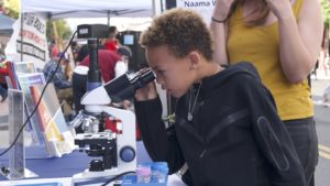 young boy looking through a microscope at an event on campus