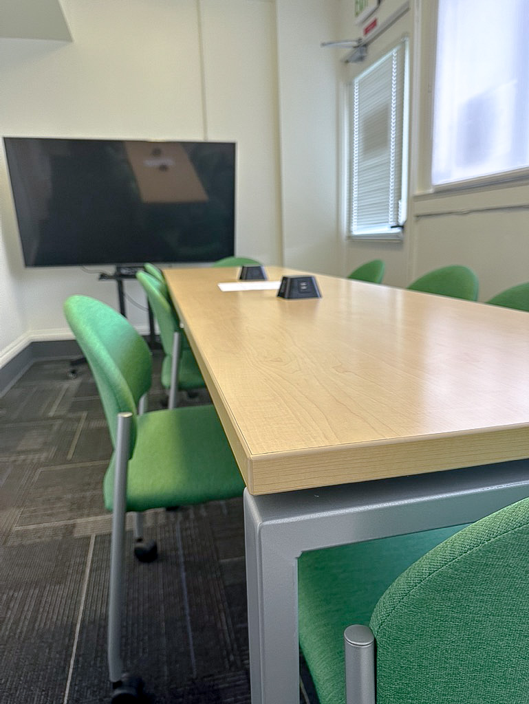 meeting room with display screen, table and green chairs
