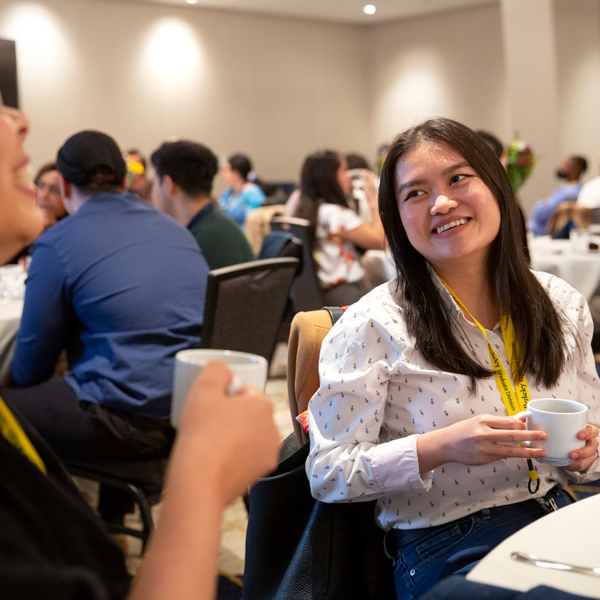 female student in white shirt smiling at another student in blue shirt while sitting at a table during a conference