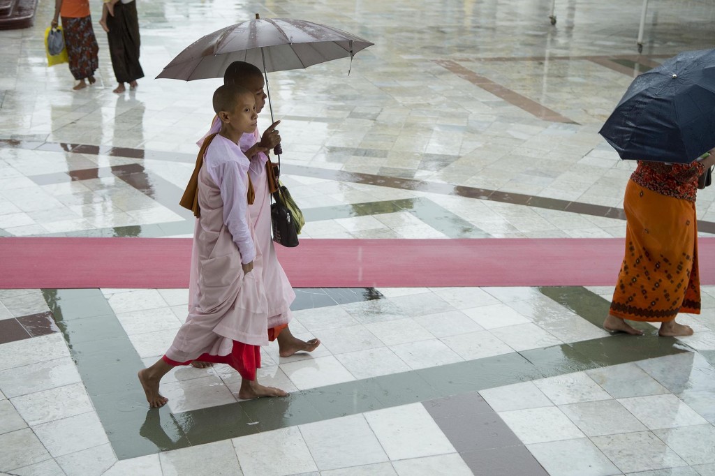 Two buddhist nuns walk through Shwedagon Pagoda in Yangon, Myanmar holding umbrellas over their heads.
