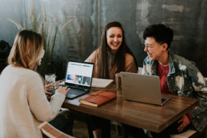 three students sitting at a table in front of laptops