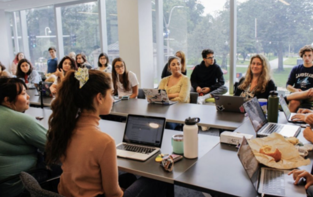 Group of students gathered around tables with laptops during a group discussions.