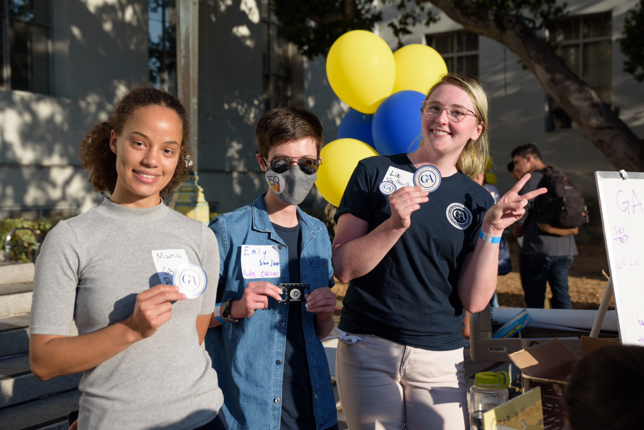 three students standing in front of yellow and blue balloons