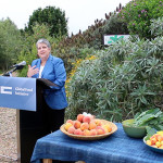 Janet Napolitano speaking in front of a garden