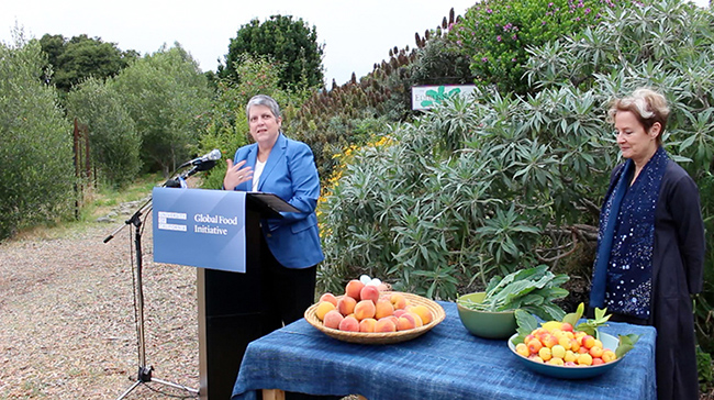 Janet Napolitano speaking in front of a garden